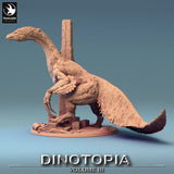 Side view of a therizinosaurus miniature standing on a debris-filled base with a stone pillar.