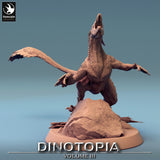Rear side view of the feathered dinosaur model showing the long tail and rocky terrain base.